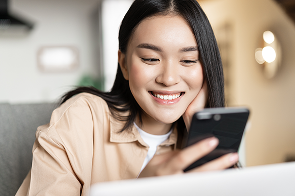 smiling-asian-girl-using-cellphone-working-on-lap-2022-03-25-15-51-28-utc